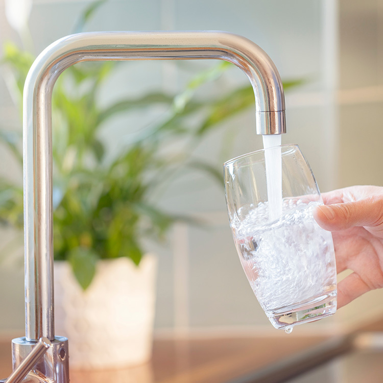Bild på en vattenkran, en person håller fram ett glas och fyller det med vatten. Visar hur man kan ha individuell mätning av vattenförbrukning.